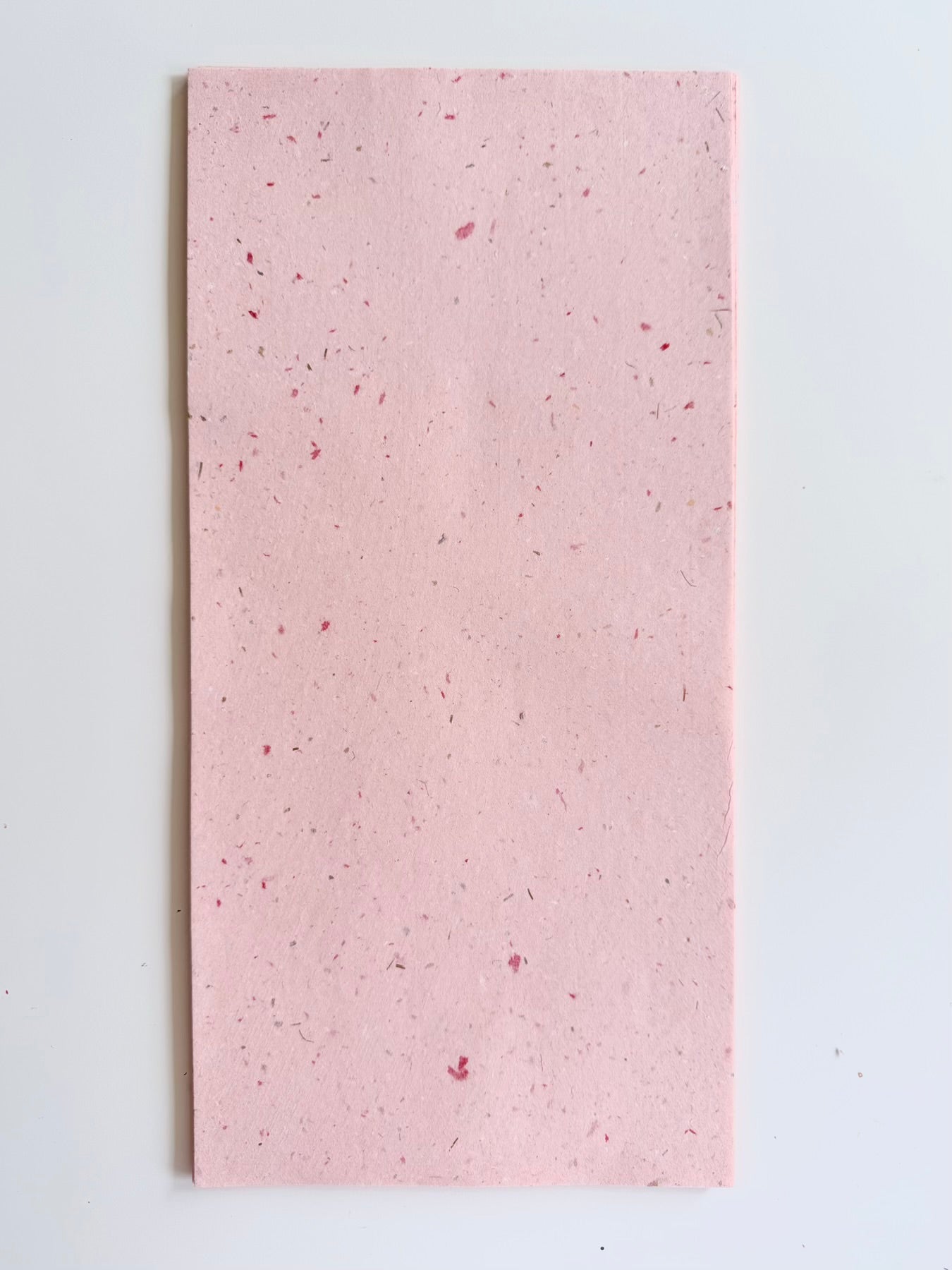 A rectangular sheet of light pink handmade mulberry paper with small red and silver speck.