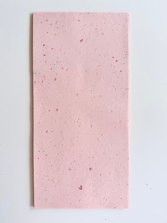 A rectangular sheet of light pink handmade mulberry paper with small red and silver speck.