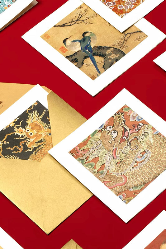 A styled greeting cards of traditional Chinese art prints with white borders, featuring dragons and a warrior scene, arranged on a deep red background with gold envelopes.
